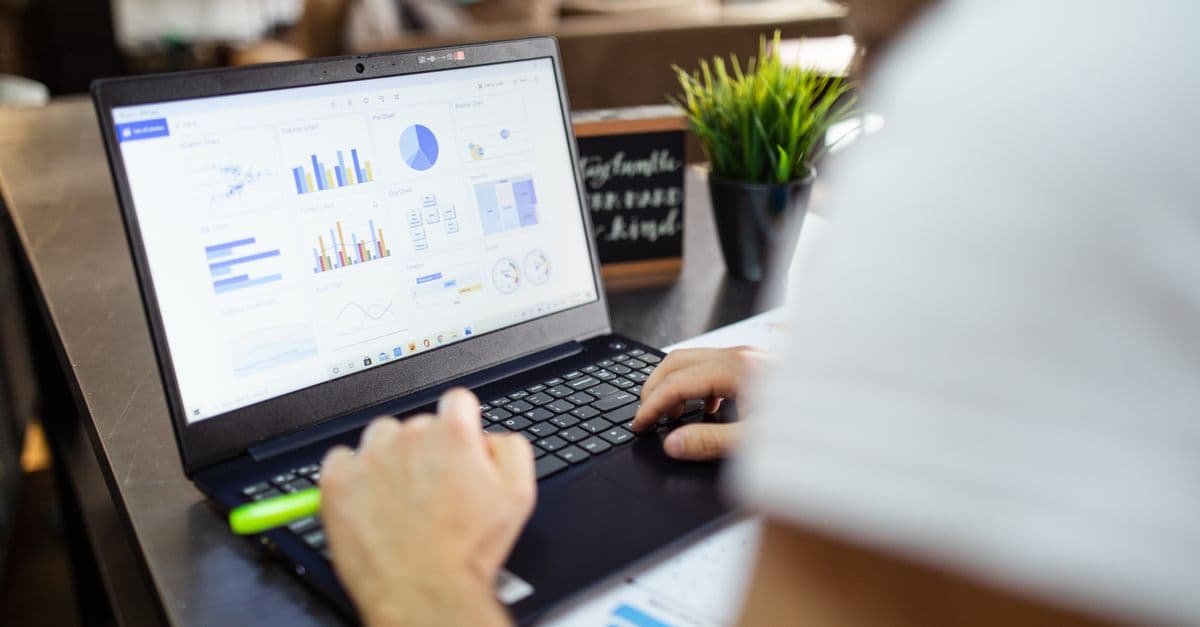 Hands on a laptop keyboard, the screen showing a gallery of chart types, with a green highlighter and a potted plant on the desk.
